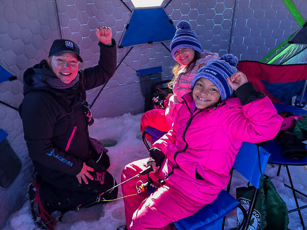 Participants smile with their fishing rods and reels while ice fishing.