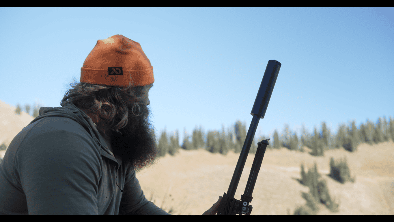 Man surveys the foothills while hunting with a silenced rifle.