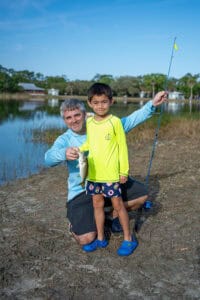 Kid and adult holding up a fish in front of a lake. 