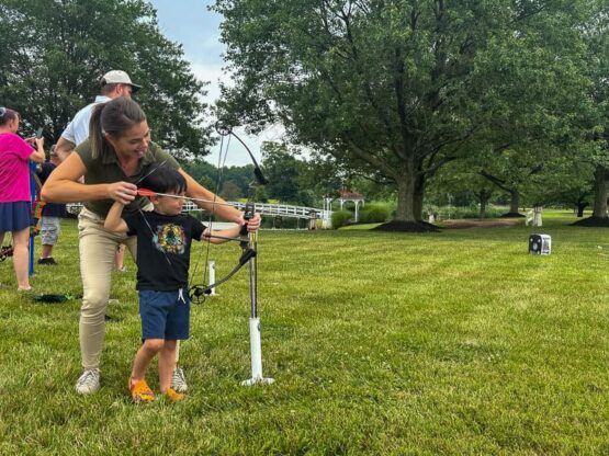 A kid shoots archery with adult